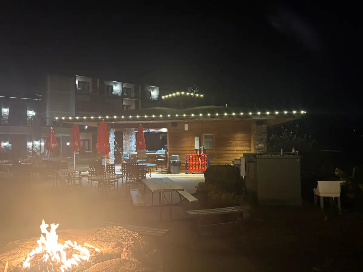 A lakeside patio with a stone fire pit burning under strung warm white lights