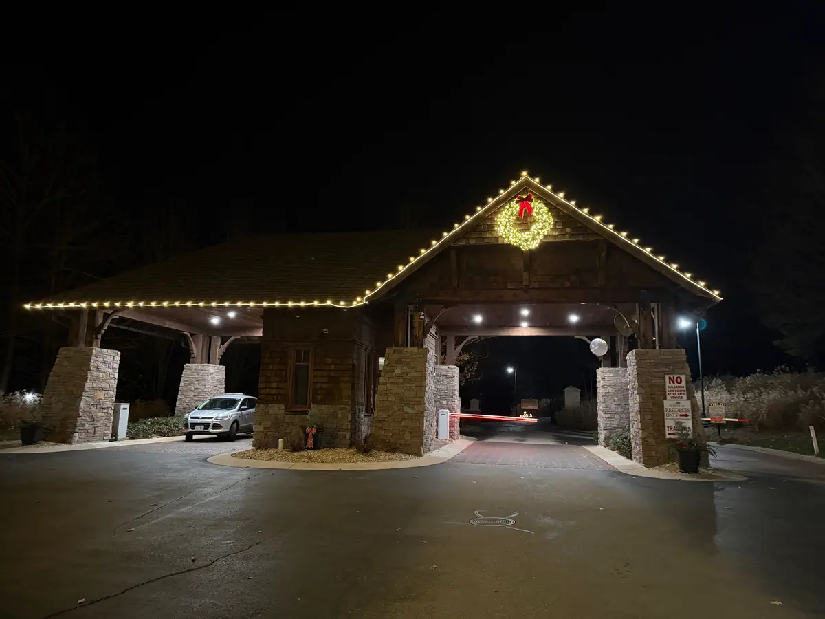 A timber and stone gatehouse with a lit wreath and warm white lights along the roofline