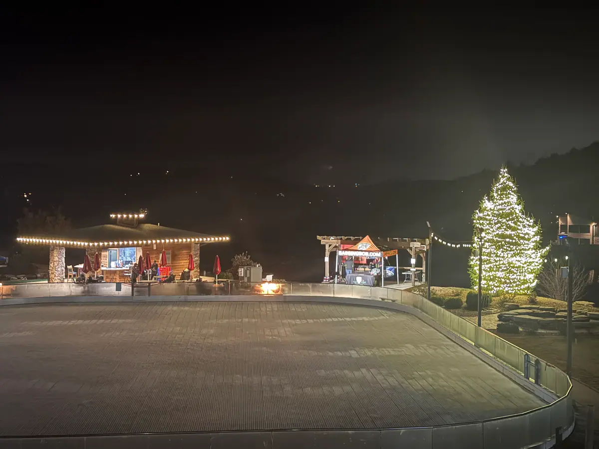 A lit evergreen and glowing pavilion across the grounds of a lakeside resort at night